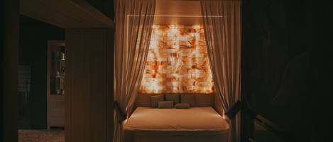 A dimly lit room with a bed, curtains, and a wall with a patterned design.