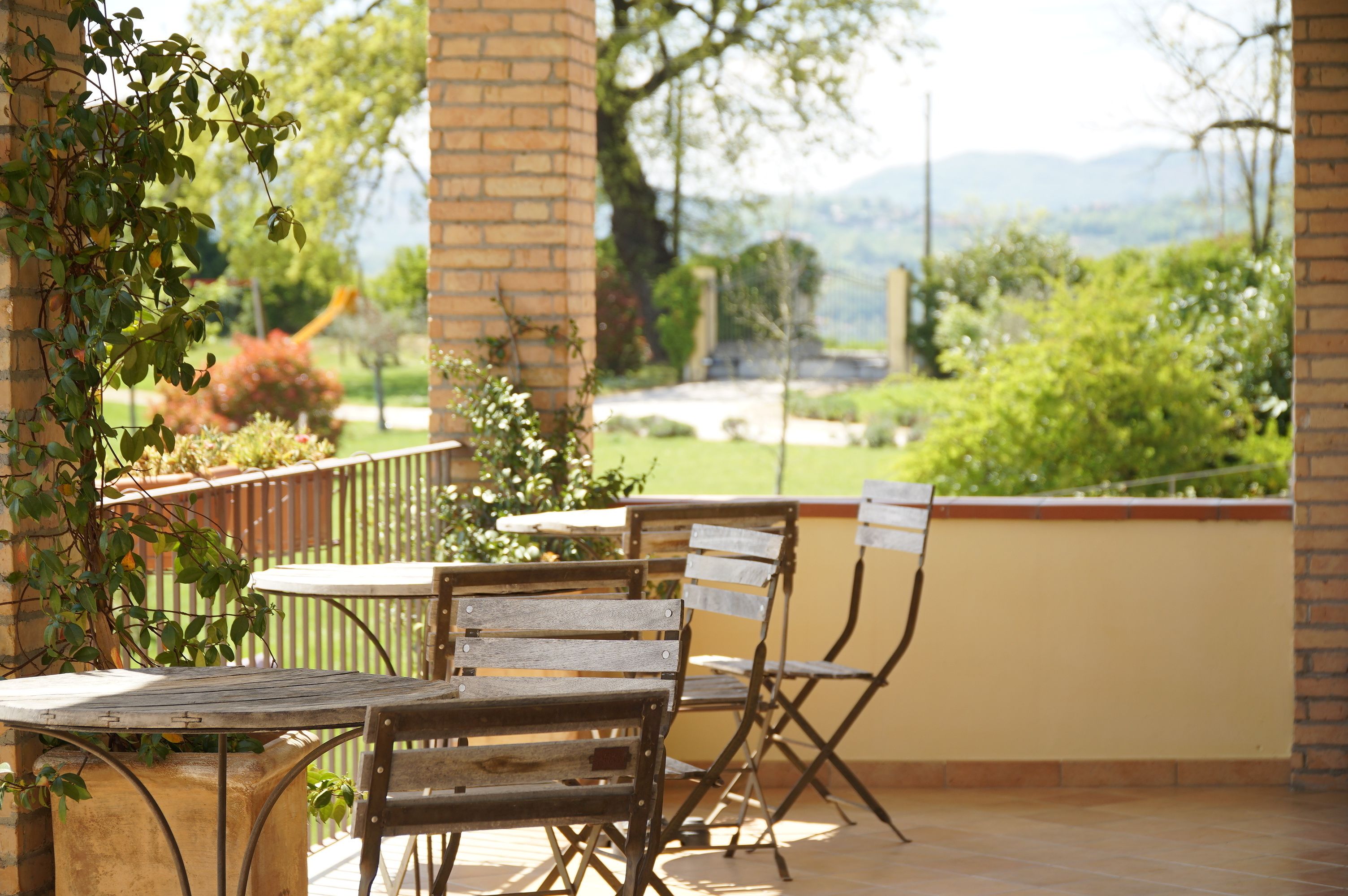 Un patio al aire libre con una mesa y sillas, un muro de ladrillo y vistas a la vegetación y montañas al fondo.