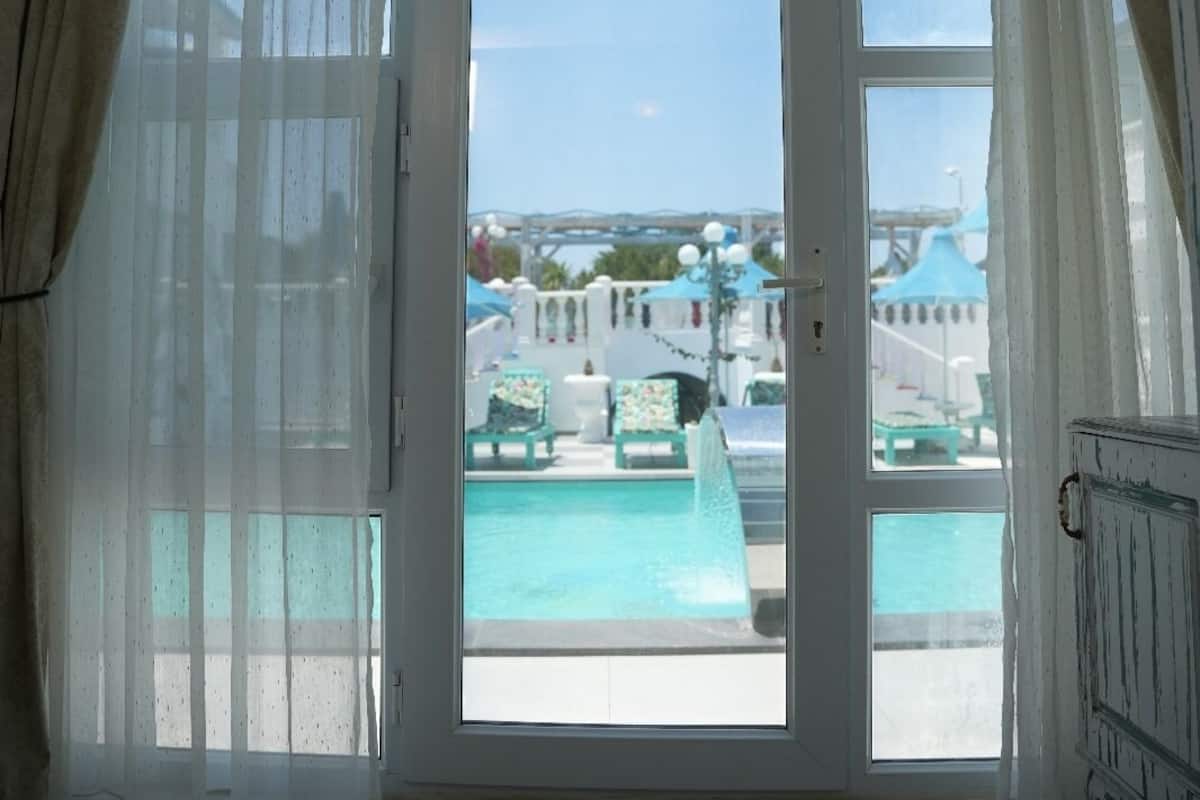 Una habitación con un amplio ventanal que da a una zona de piscina, una lámpara en el techo y vistas a la piscina y al mobiliario exterior.