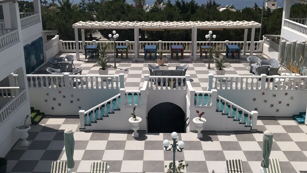 Zona junto a la piscina con suelo a cuadros, sillas de descanso y vista al mar.