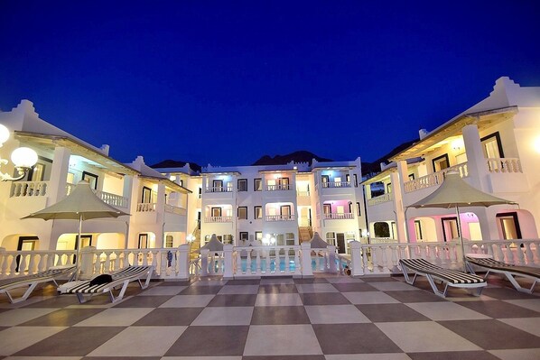 A hotel courtyard with a checkered floor, multiple balconies, and outdoor seating areas. - Bahama Art Hotel (Bodrum)