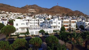 Un pueblo costero con edificios blancos, una montaña al fondo y una bandera en la cima.