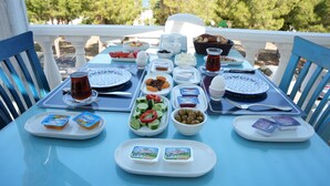 Una mesa dispuesta con diversos alimentos y bebidas, incluyendo platos de aceitunas, pepinos y queso, y un vaso de bebida roja.