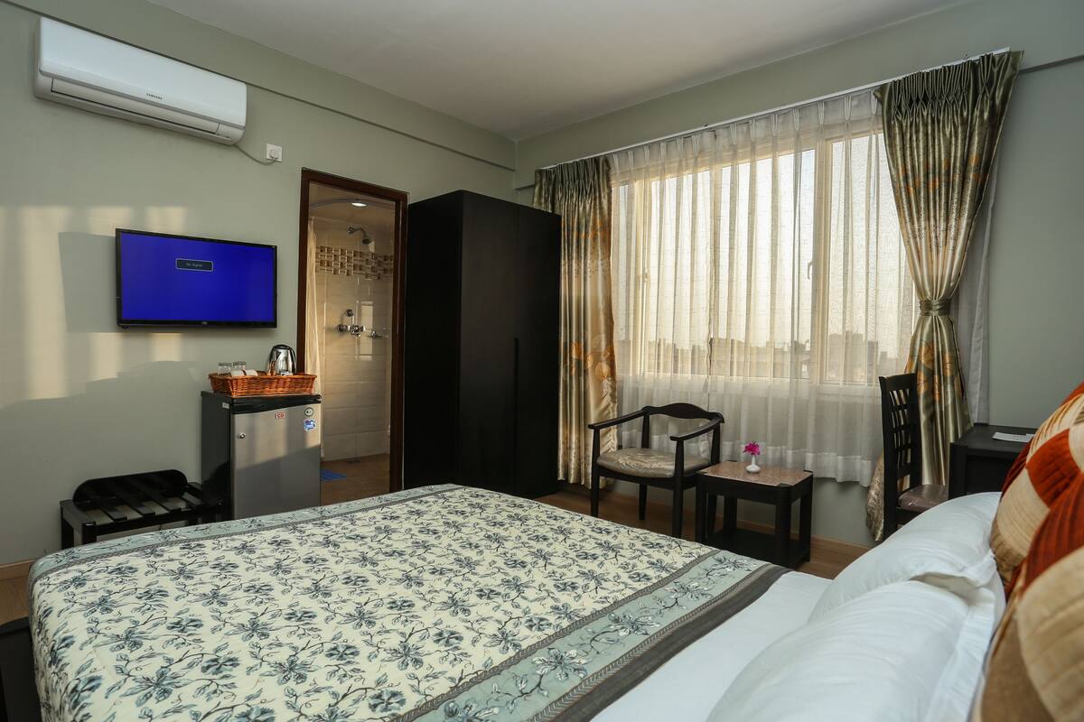Una habitación de hotel con cama, televisión, escritorio, silla y ventana con cortinas.