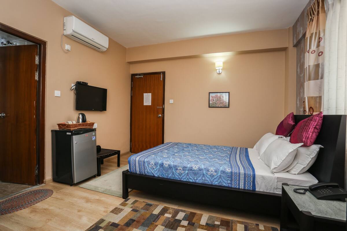 Un dormitorio con cama, escritorio, refrigerador, televisor y una puerta.