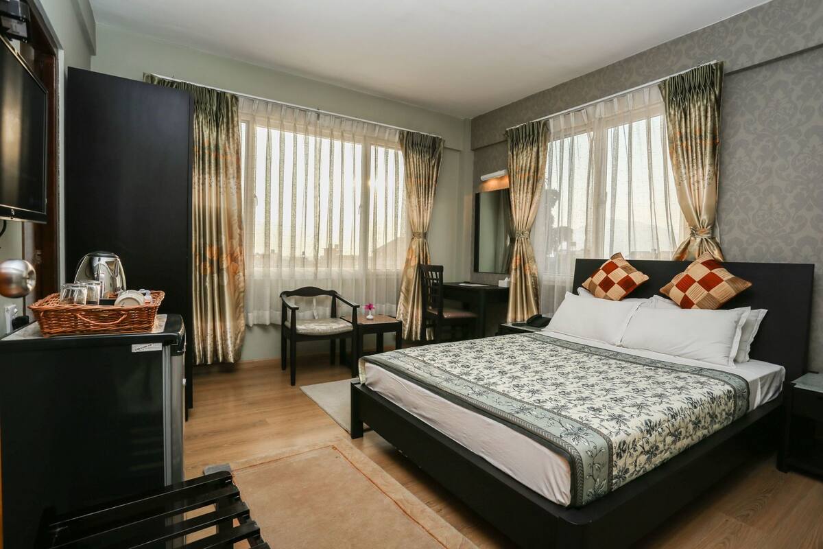 Una habitación de hotel con cama, escritorio, silla, televisión y cortinas.