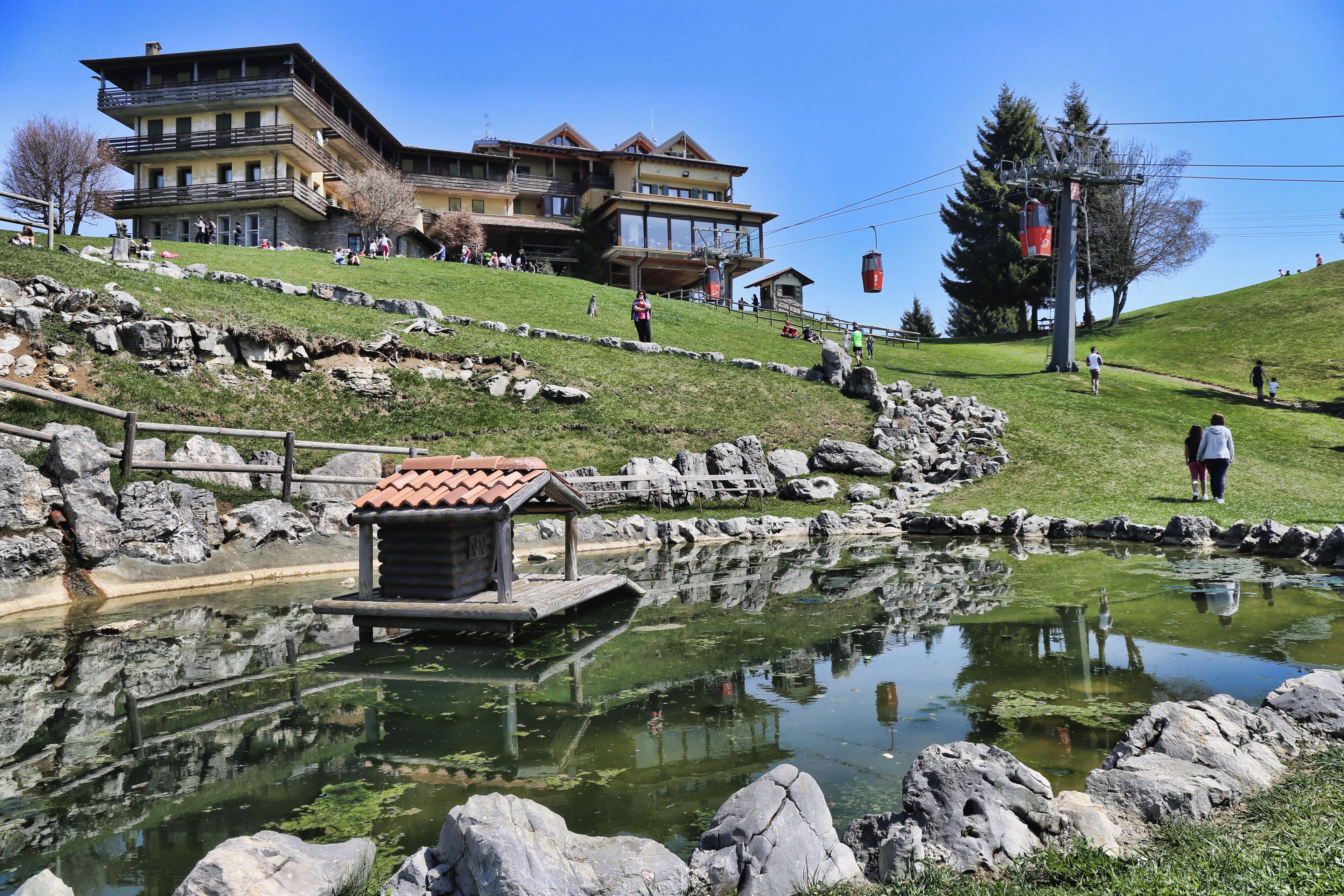 A lakeside view with a wooden dock, a small wooden structure, and a building with multiple balconies in the background.