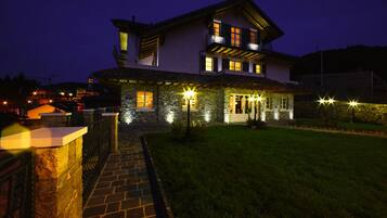 A two-story house with a stone facade, a balcony, and a well-lit entrance.