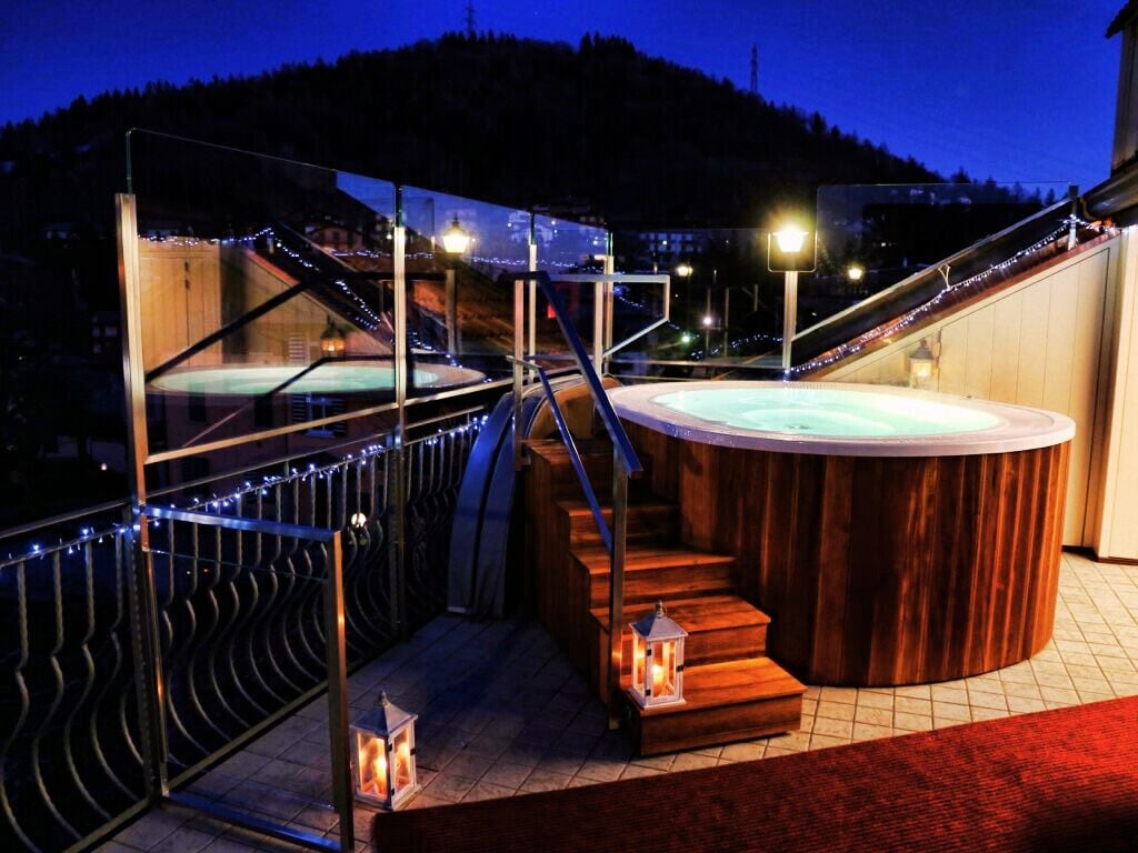 Un jacuzzi con revestimiento de madera, rodeado por una barandilla de vidrio y escalones de madera.
