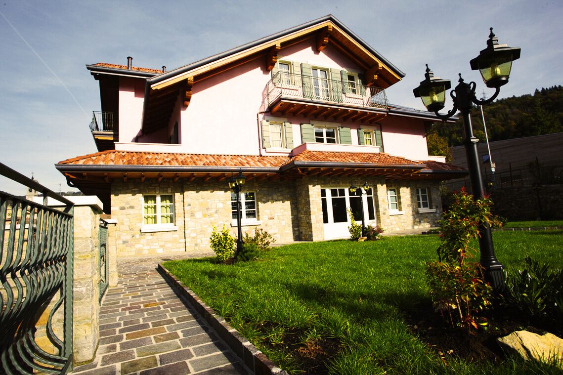 Ein zweistöckiges Steinhaus mit Ziegeldach, Balkon und gepflastertem Eingangsbereich.