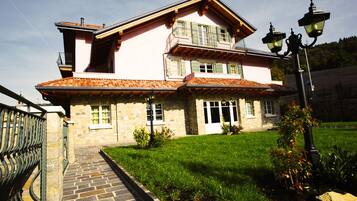 Ein zweistöckiges Steinhaus mit Ziegeldach, Balkon und gepflastertem Eingangsbereich.