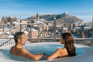 Una pareja en un jacuzzi con un pueblo nevado al fondo.