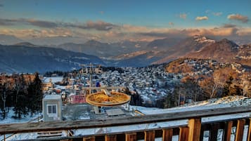 Une vue panoramique d’une ville de montagne, avec une grande roue bien visible, des bâtiments recouverts de neige et un ciel dégagé.