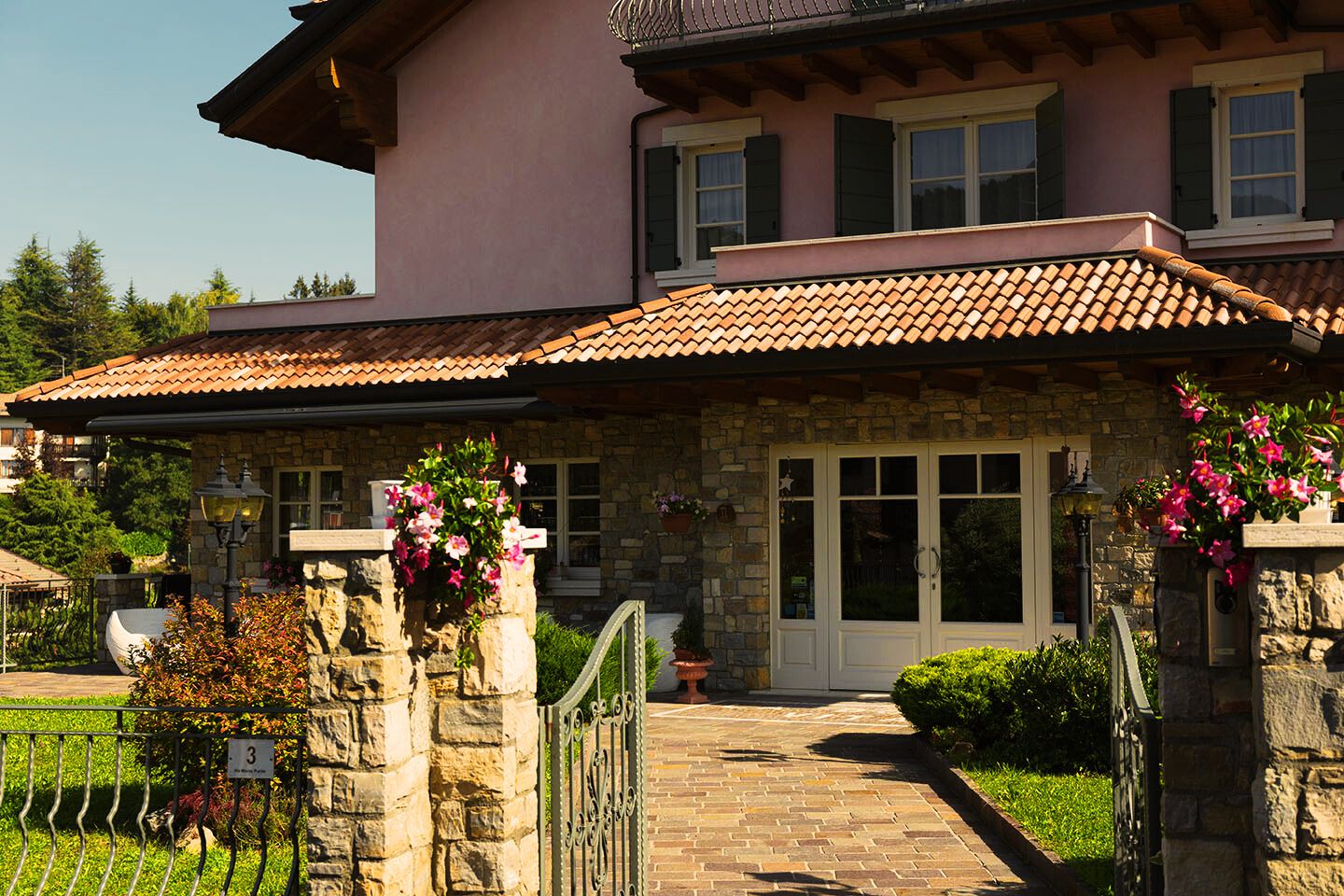 Una casa de piedra con tejado de baldosas, una puerta principal y un pequeño jardín con macetas y flores.