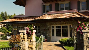 Una casa de piedra con tejado de baldosas, una puerta principal y un pequeño jardín con macetas y flores.