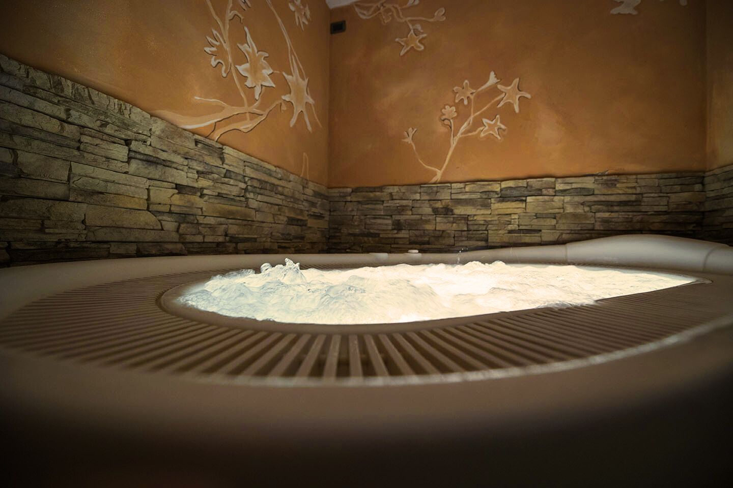 A hot tub with a stone wall and floral wall art.