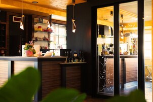 Una zona de bar moderna con detalles de madera, lámparas colgantes y un separador de vidrio.