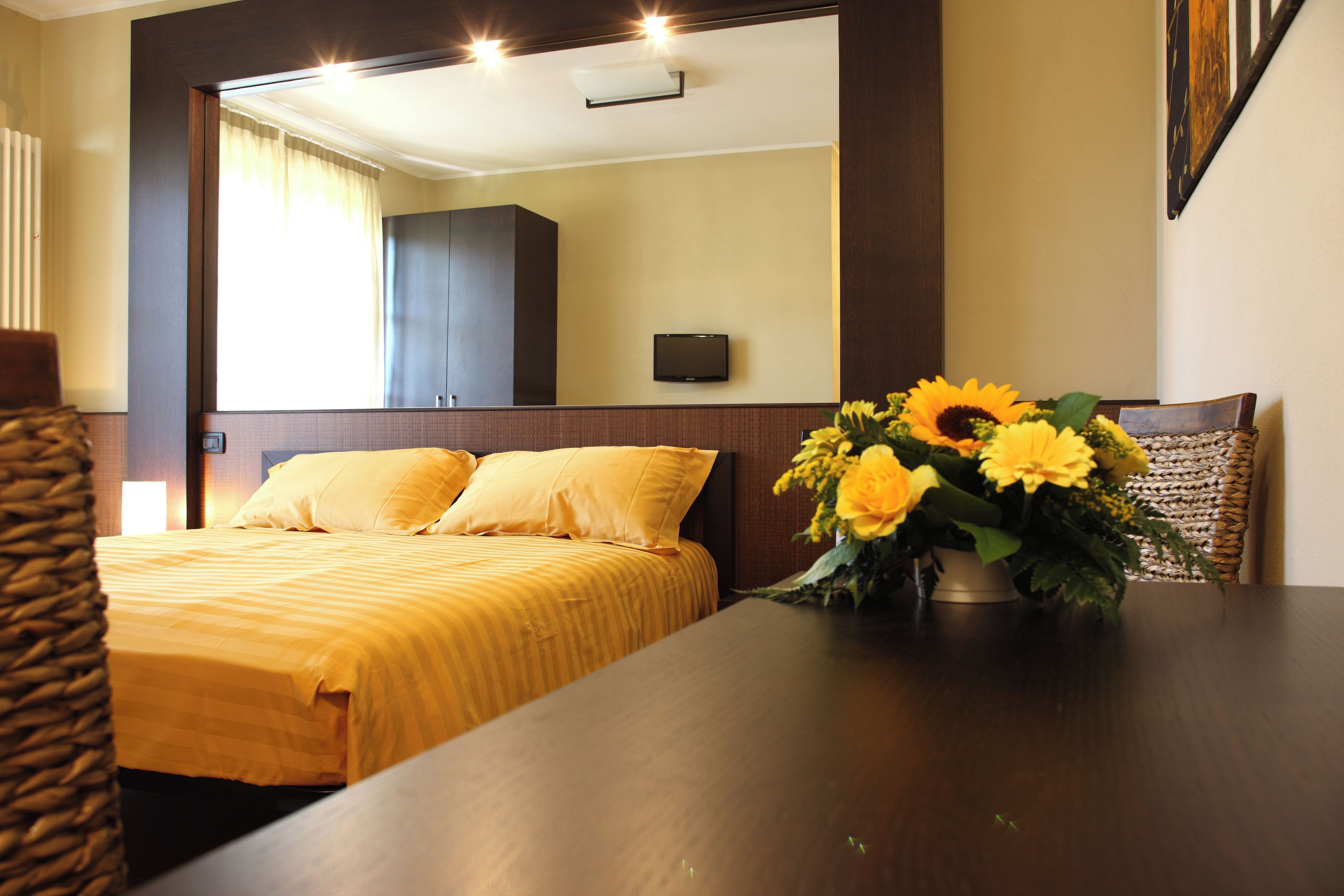 A hotel room with a bed, a flat-screen TV mounted on the wall, and a vase with flowers on the table.