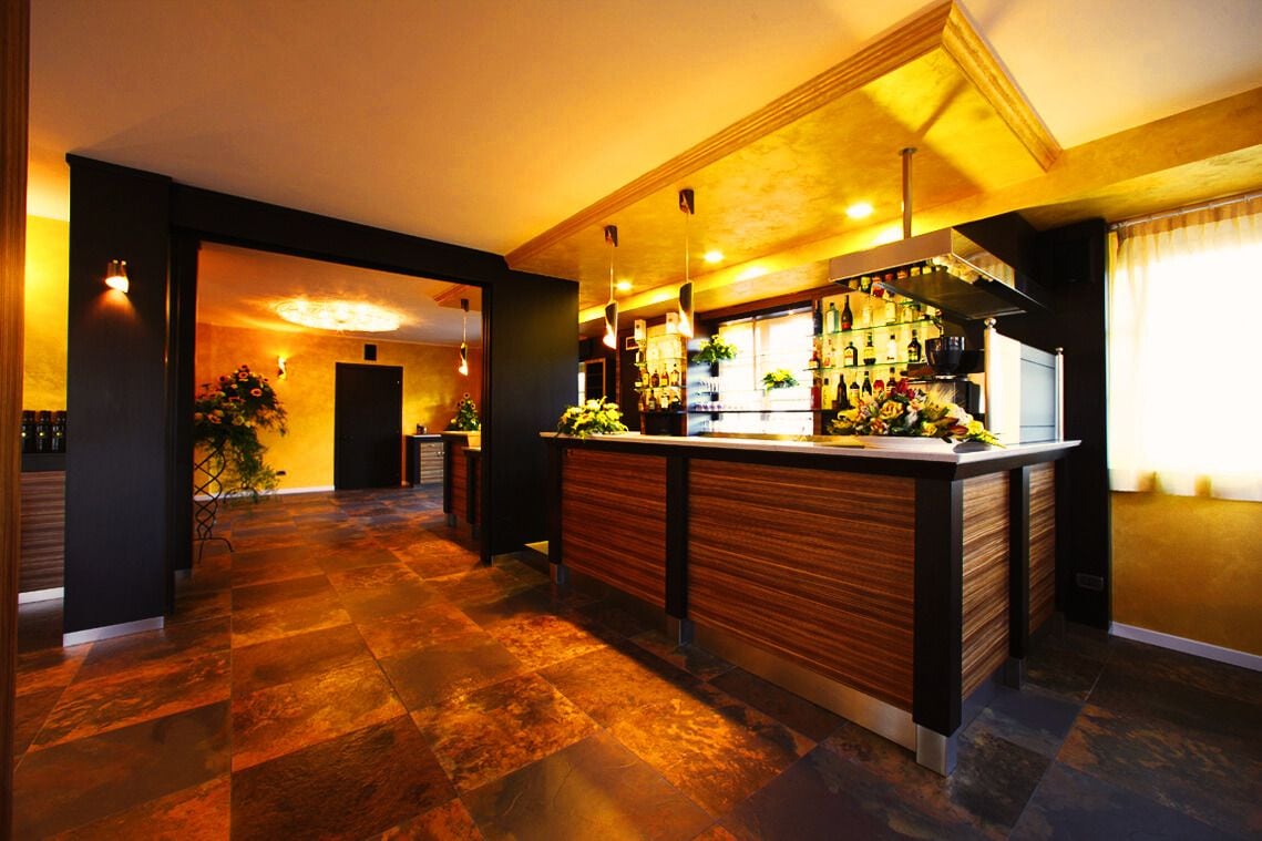 Un área de bar moderna con una barra de madera, iluminación ambiental y piso a cuadros.