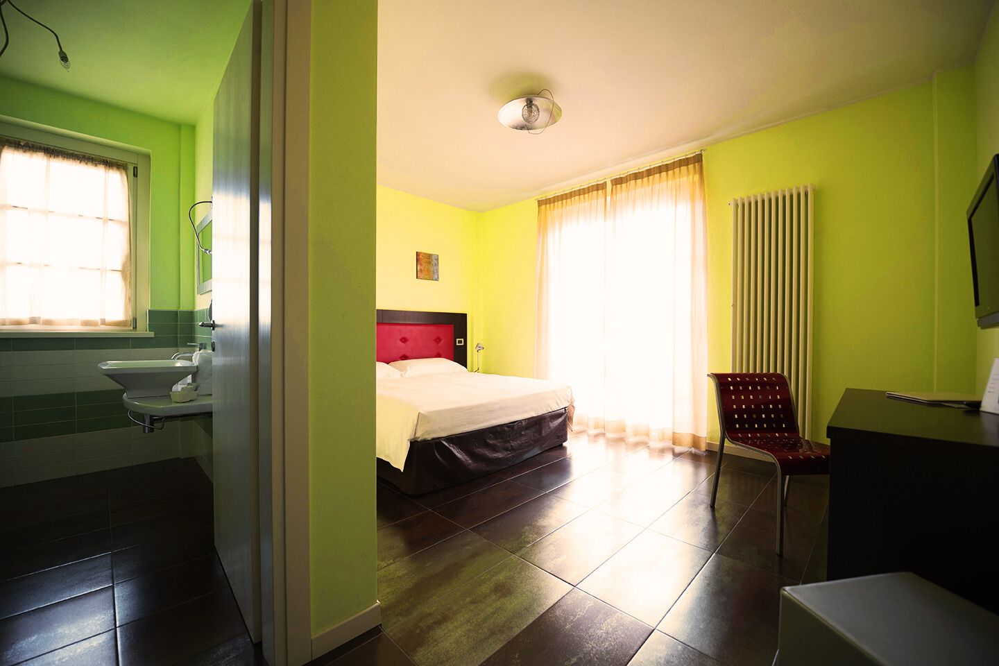 Una habitación de hotel con cama, una silla, un escritorio y un baño con lavamanos e inodoro.
