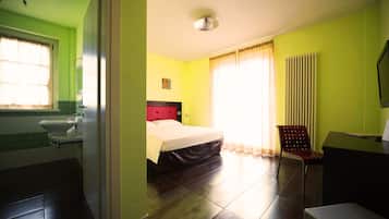 Una habitación de hotel con cama, una silla, un escritorio y un baño con lavamanos e inodoro.