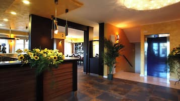 A hotel lobby with a reception desk, a staircase, and a dining area.