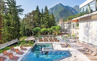 Un área de piscina en la azotea con sillas de descanso, barandilla de cristal y montañas al fondo.