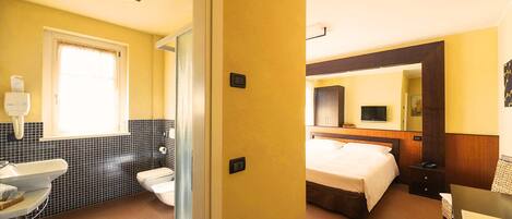 Quarto de hotel com banheiro, cama, televisão e escrivaninha.