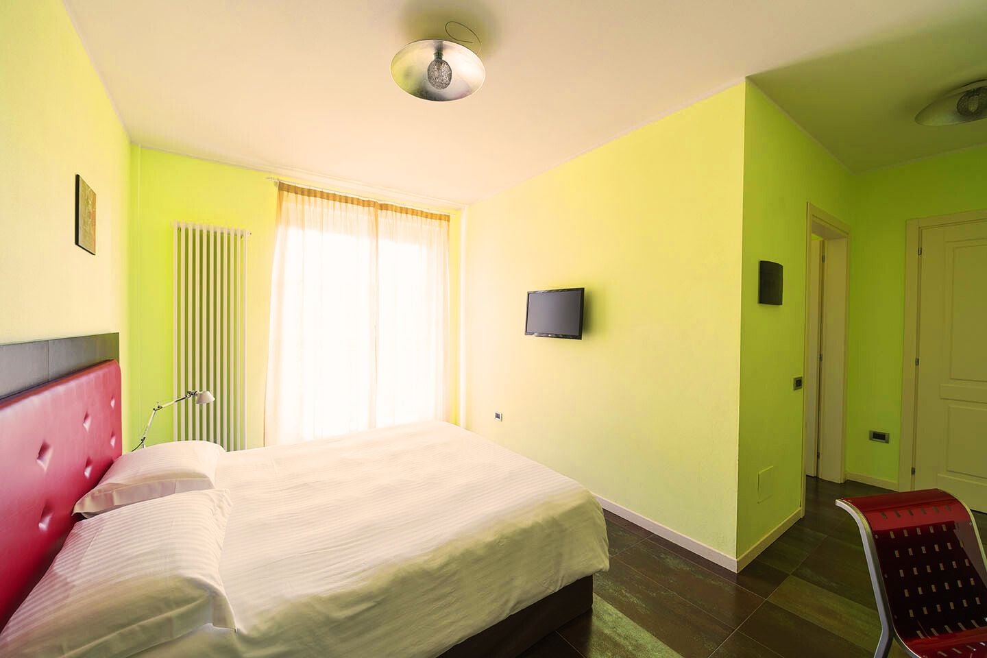 A hotel room with a bed, a television, a radiator, and a window with curtains.