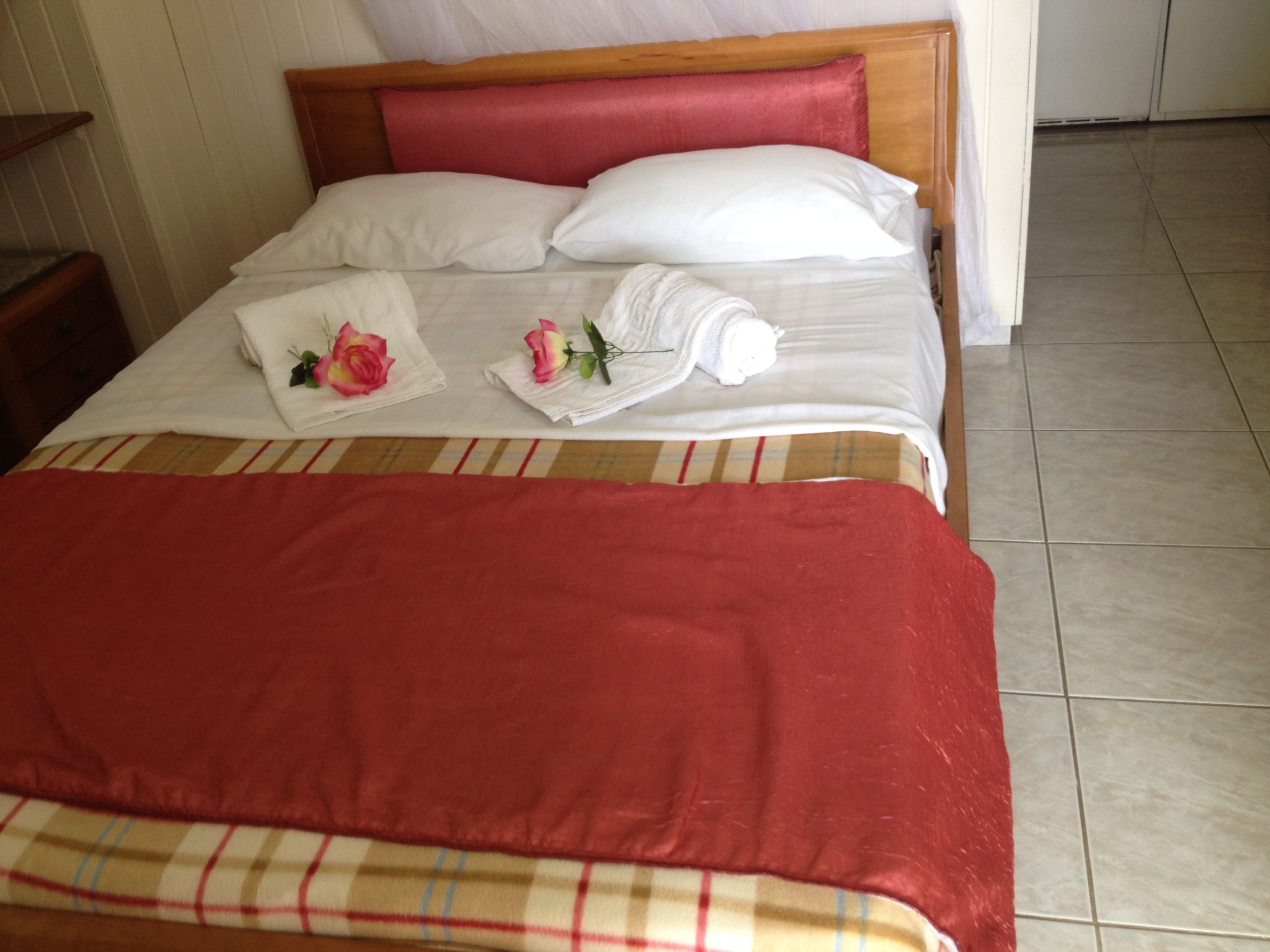 A neatly made bed with a red blanket, two white pillows, and a red headboard.