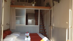 A bedroom with a bed, a window, a staircase, and a small balcony. - Alkyonis Apartments (Kalymnos)