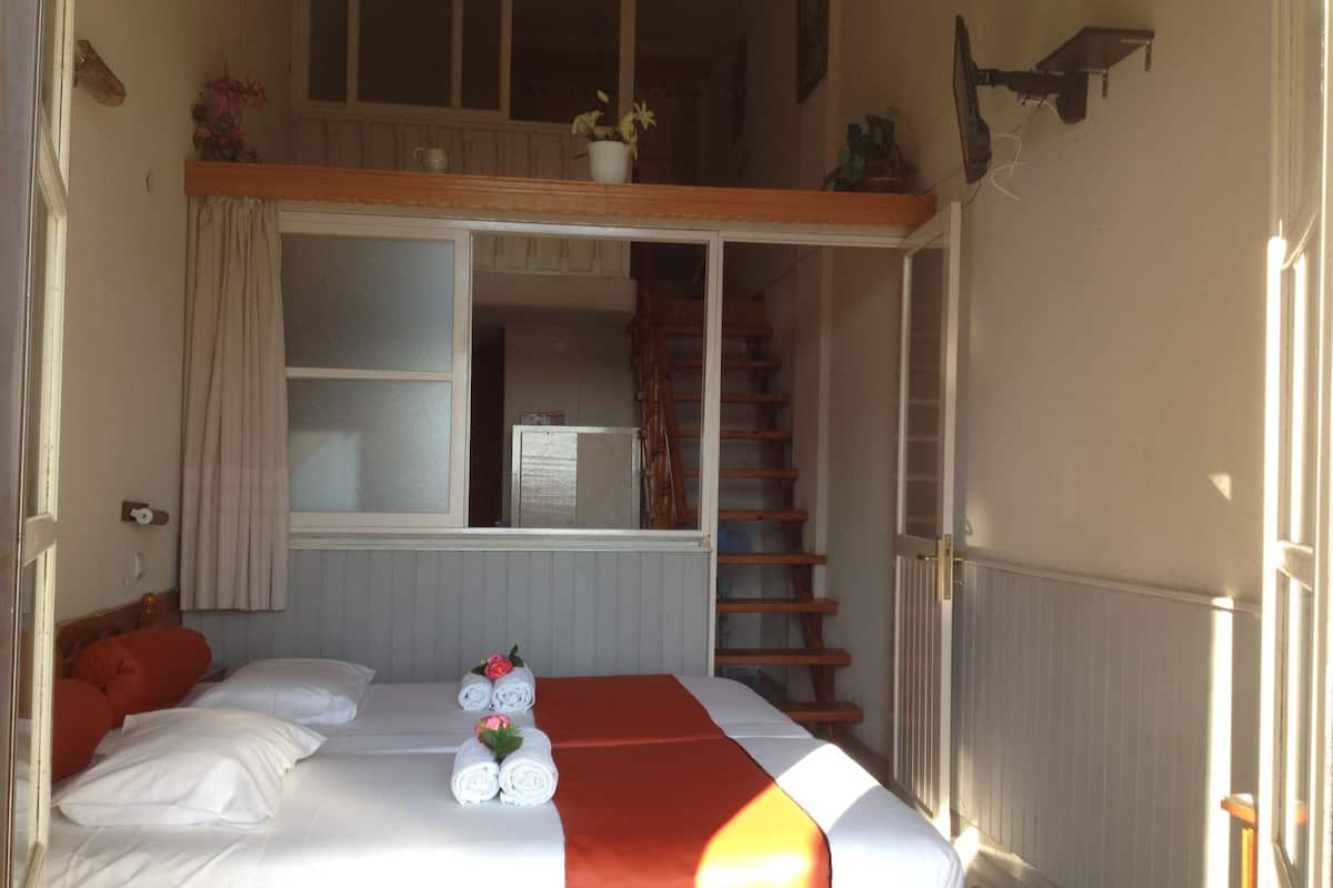 A bedroom with a bed, a window, a staircase, and a small balcony.
