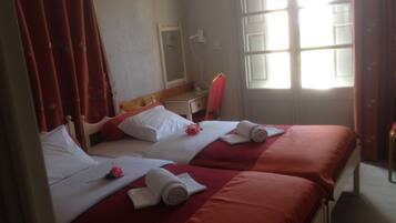 Quarto de hotel com duas camas, roupa de cama vermelha, almofadas brancas e uma janela com cortinas.