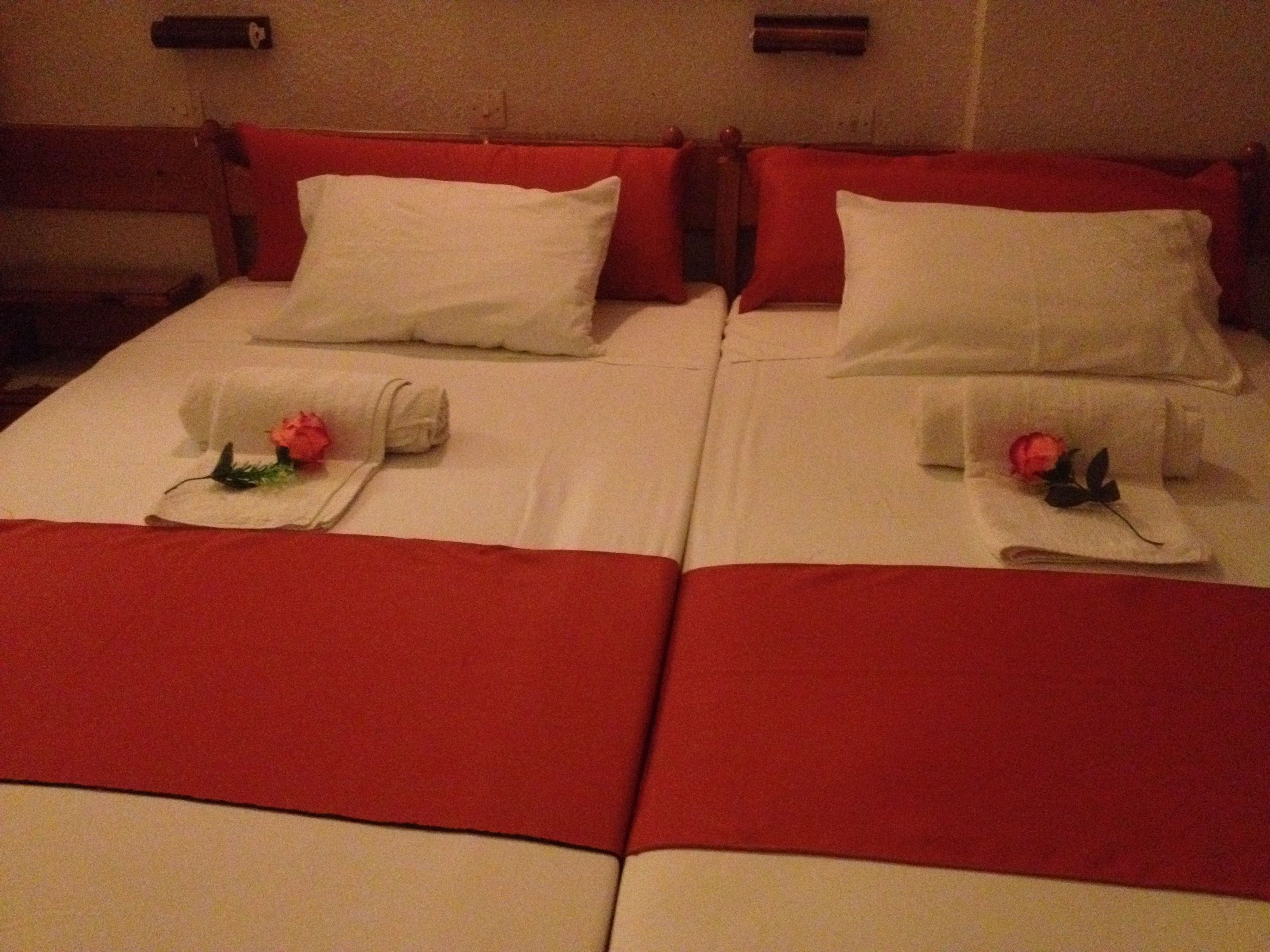Uma cama de casal com roupa de cama vermelha e branca, duas almofadas e duas toalhas com flores.