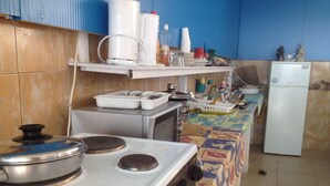 A kitchen with a stove, sink, and refrigerator. There are various kitchen utensils and appliances on the countertops. - Alkyonis Apartments (Kalymnos)