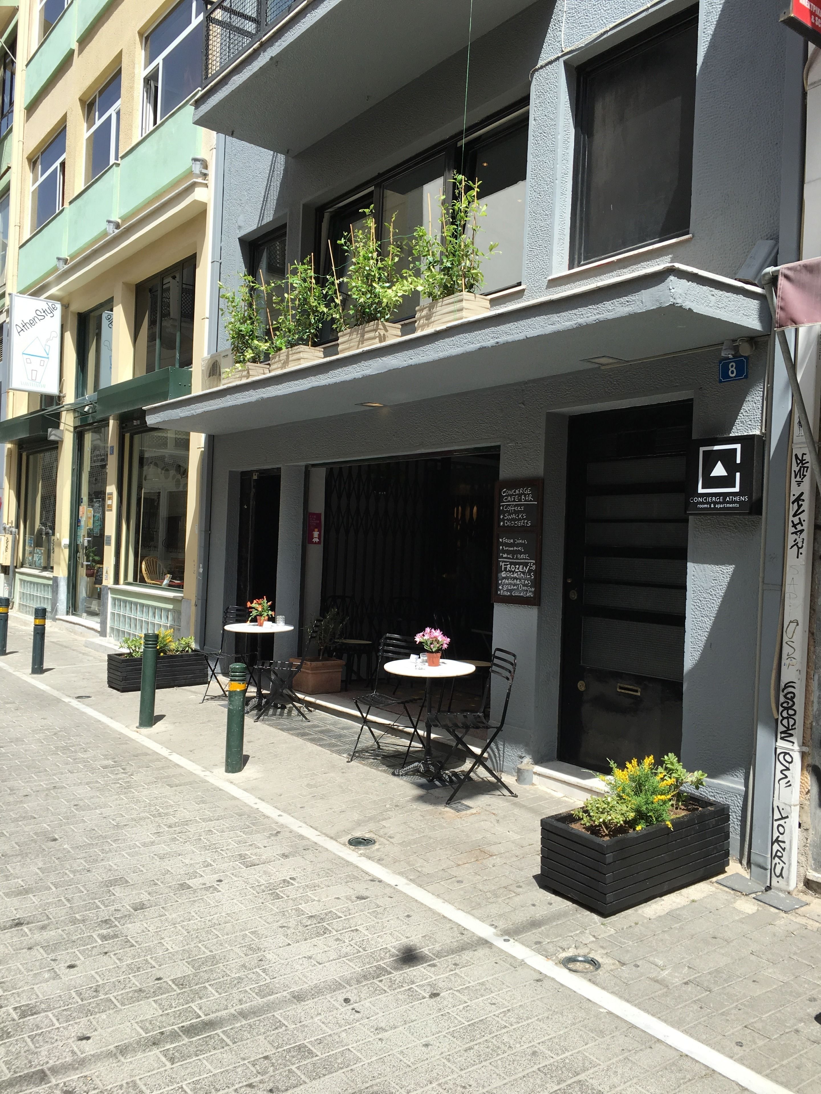 Un immeuble avec un café au rez-de-chaussée, des places assises en plein air et un panneau indiquant la présence d’un service de conciergerie.