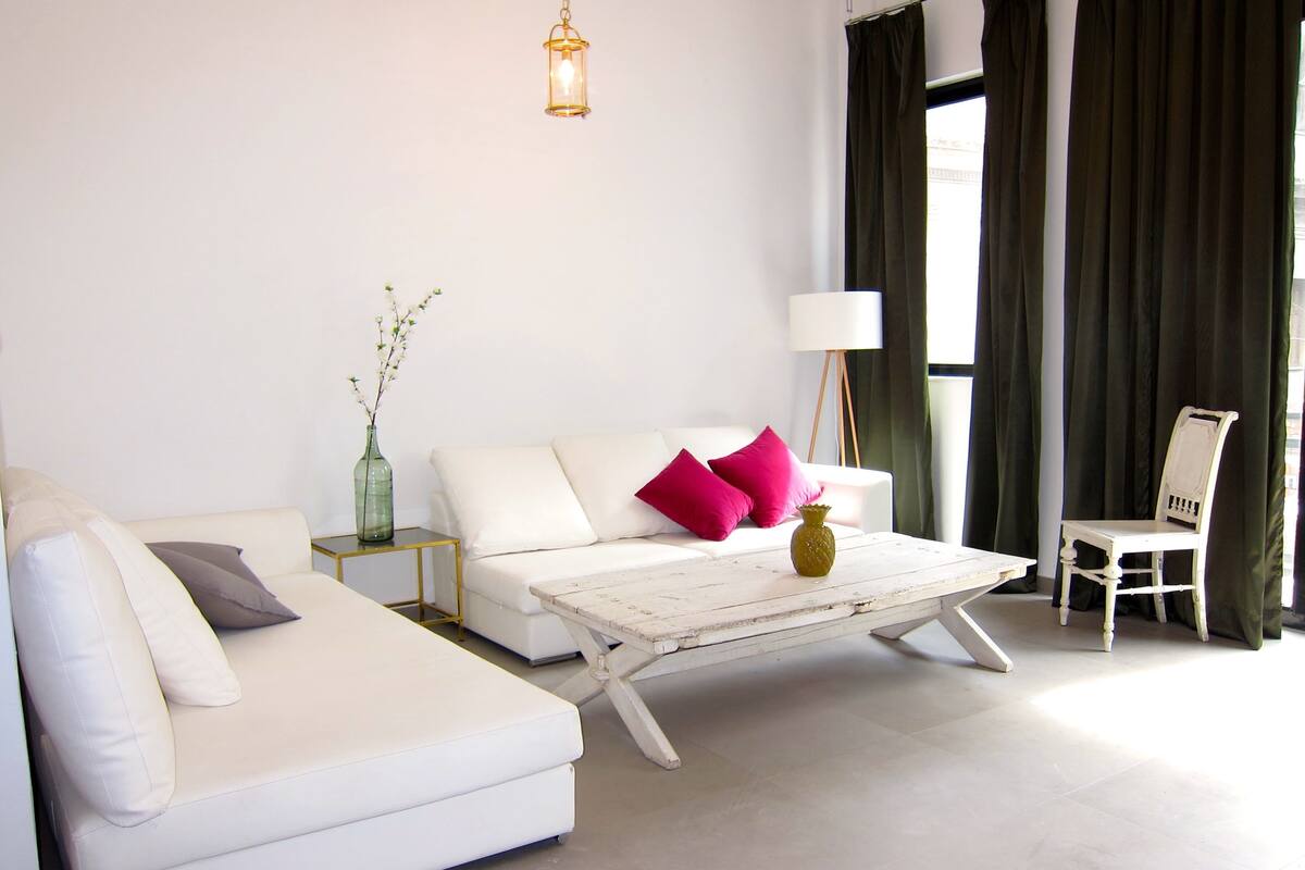 A modern living room with a white sofa, a coffee table, a lamp, and a chair.