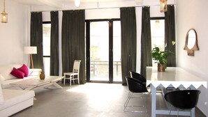 Una sala de estar moderna con un sofá blanco, una mesa de comedor con sillas, una planta en maceta y un ventanal con cortinas.