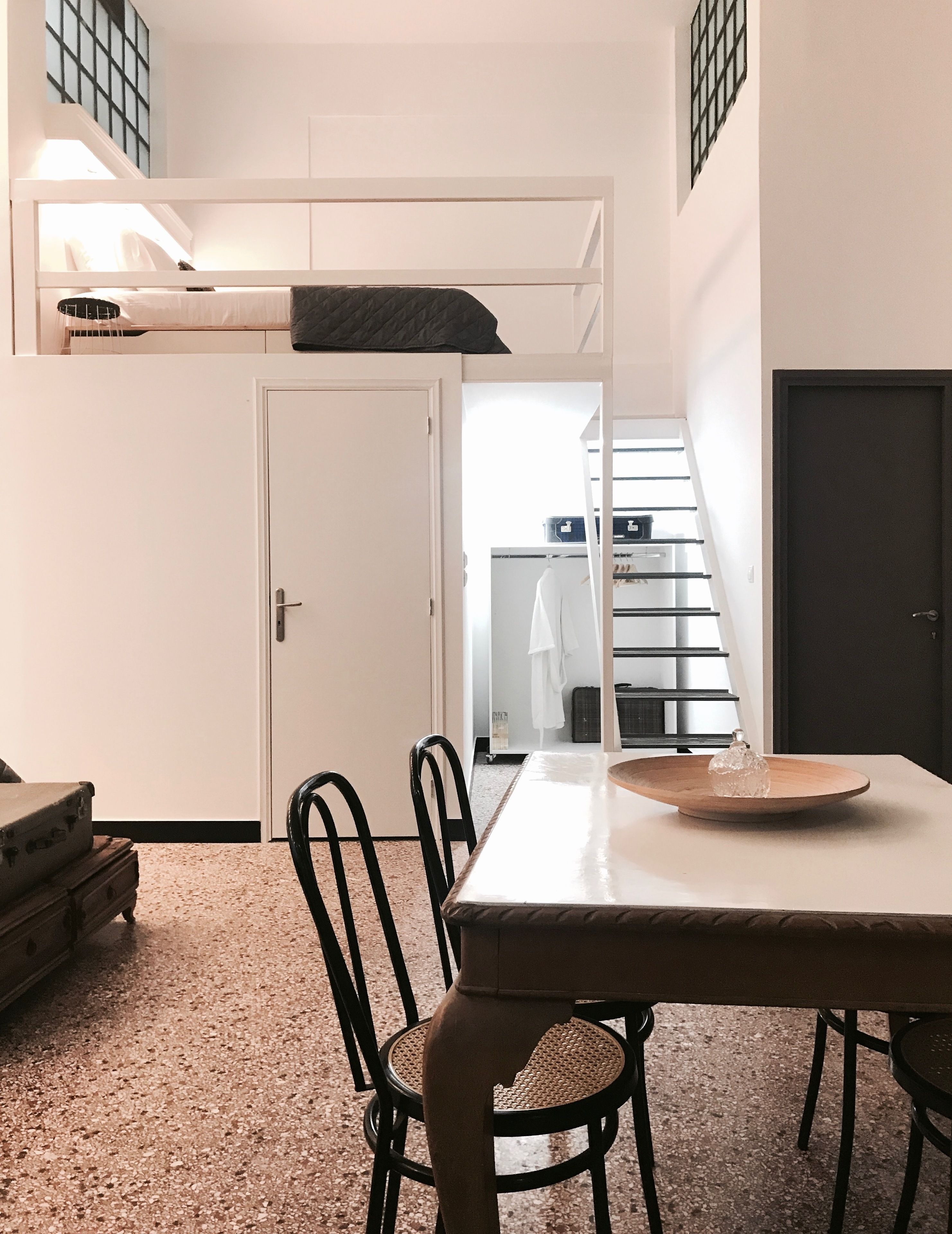 A compact room with a bunk bed, a dining table with chairs, and a suitcase.