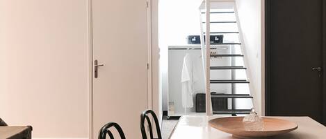 A compact room with a bunk bed, a dining table with chairs, and a suitcase.