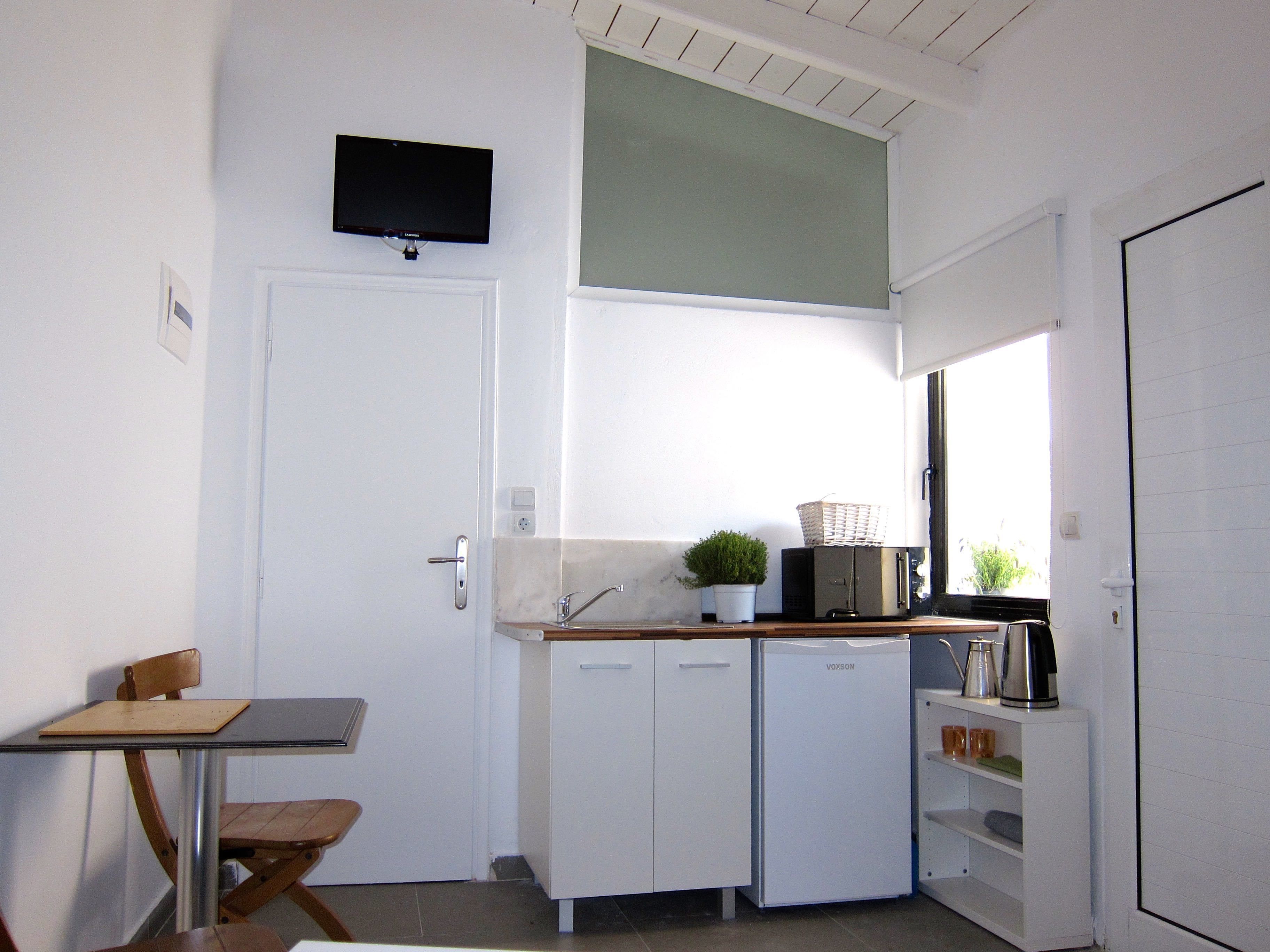 A compact kitchen with a sink, cabinets, a small table, and a television mounted on the wall.