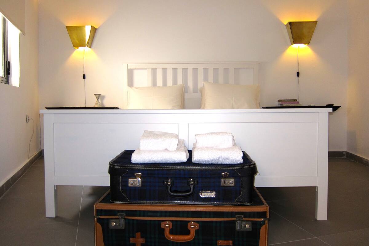 A hotel room with a bed, bedside lamps, a nightstand, and two suitcases.
