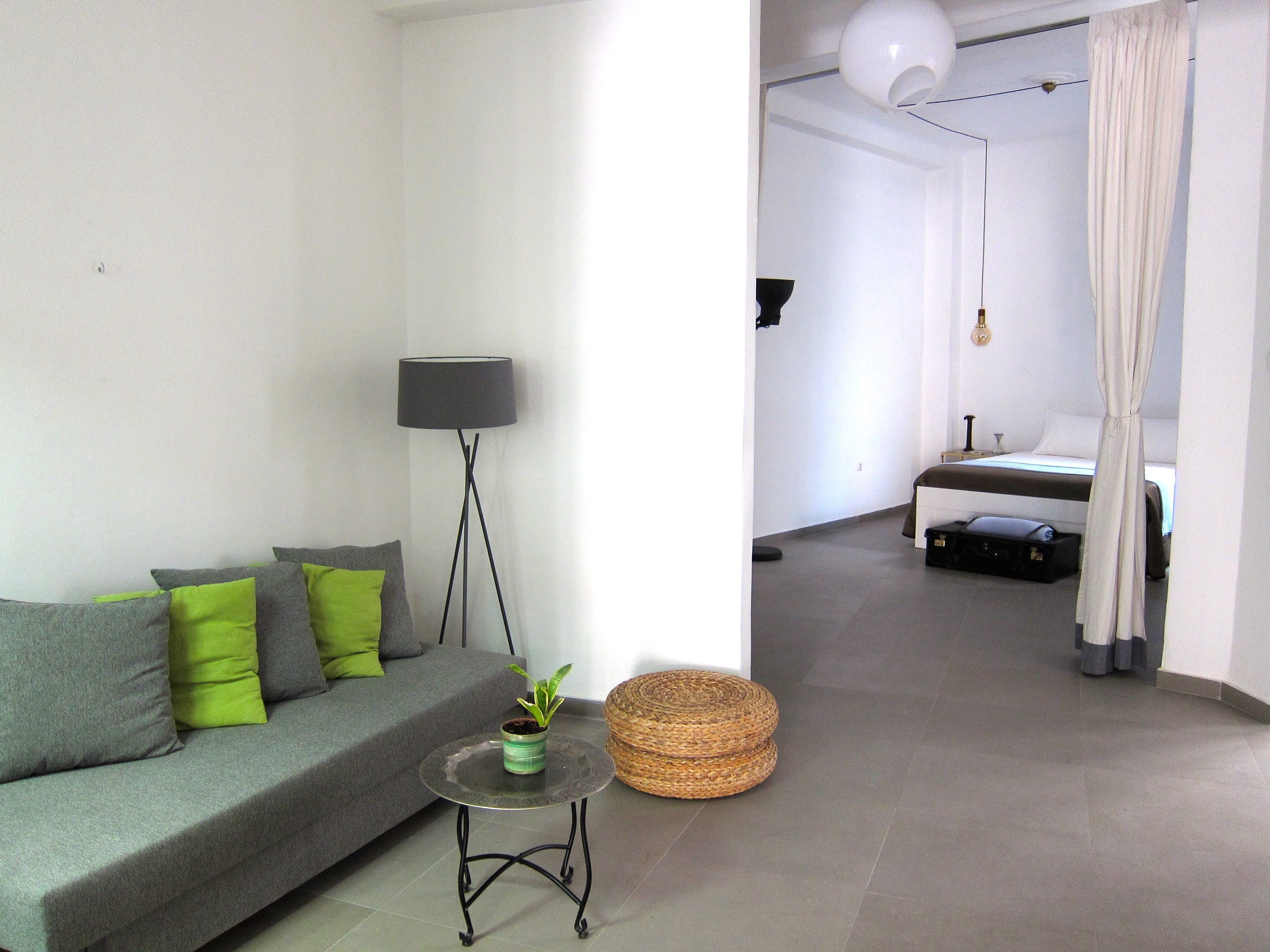 A modern living room with a grey sofa, green cushions, a floor lamp, a small table with a plant, and a wicker basket.