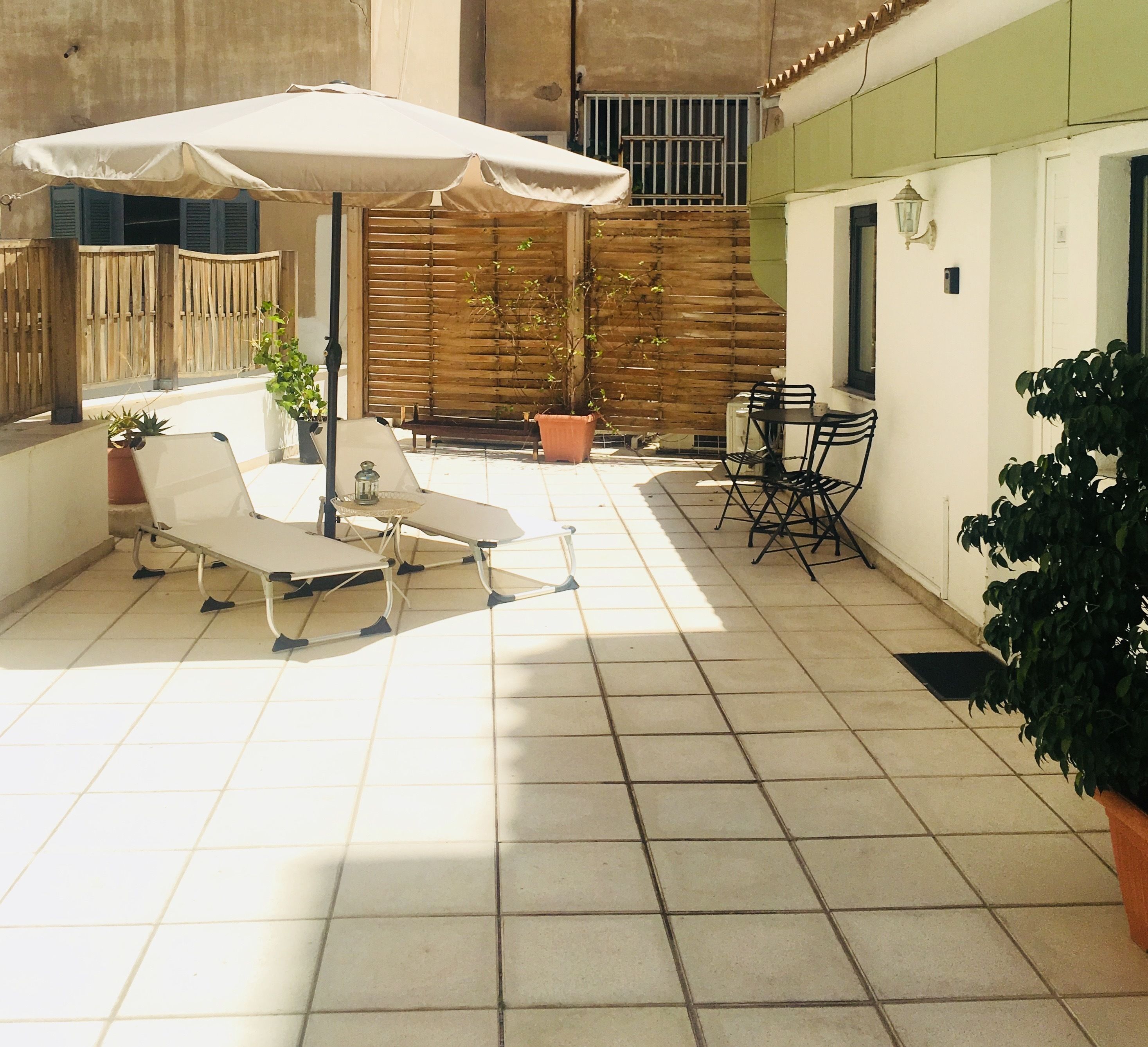 Un patio con suelo de baldosas, una sombrilla blanca y mobiliario exterior.