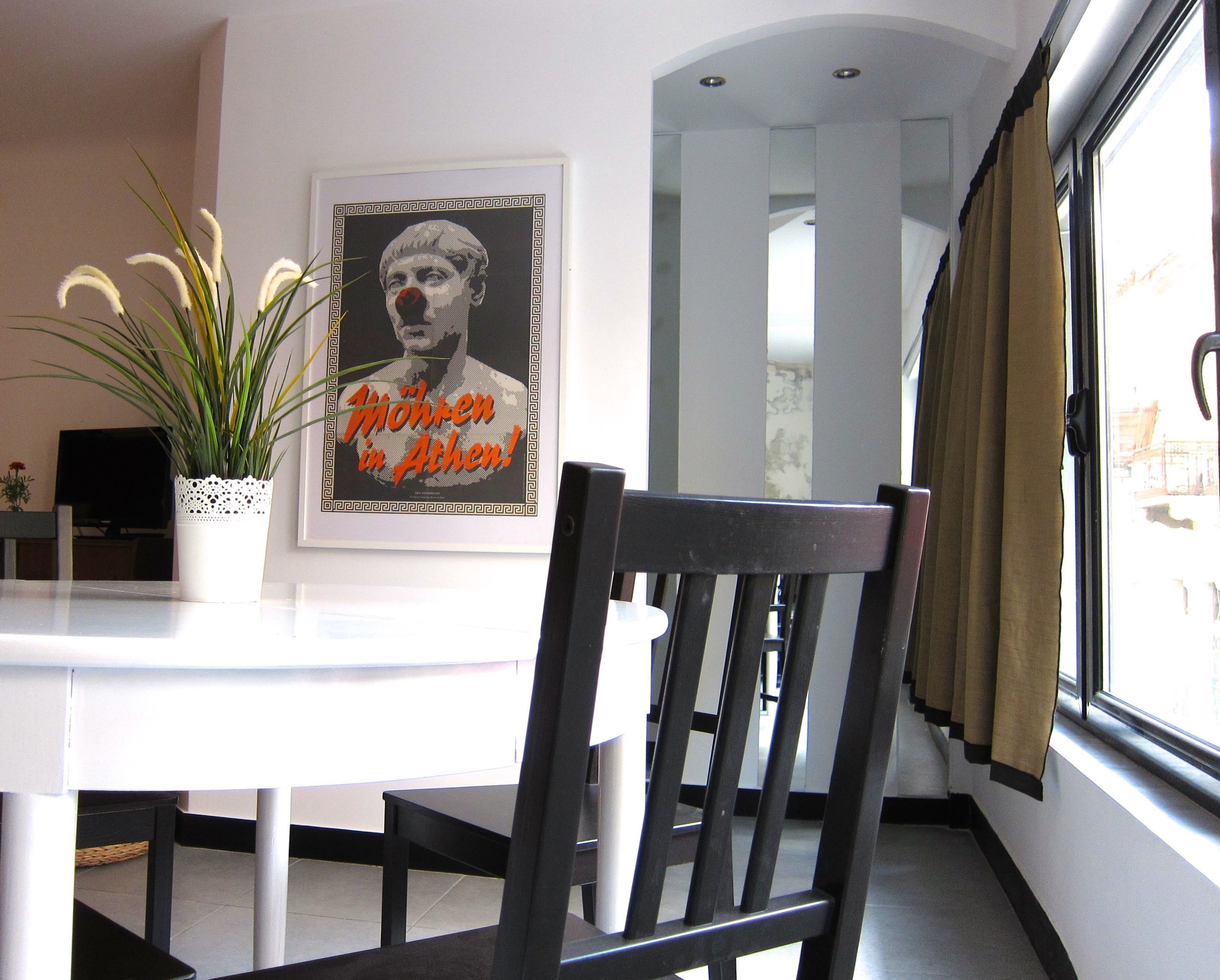 A dining area with a white table, a black chair, a potted plant, and a framed picture on the wall.