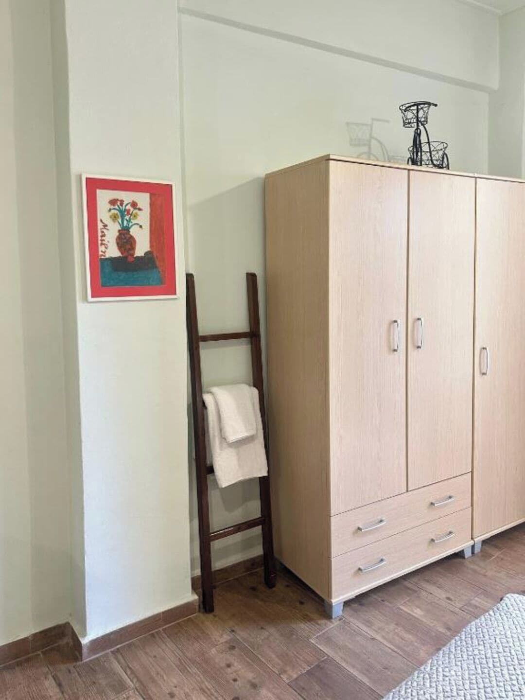 A room with a wooden wardrobe, a wooden ladder, and a framed picture on the wall.