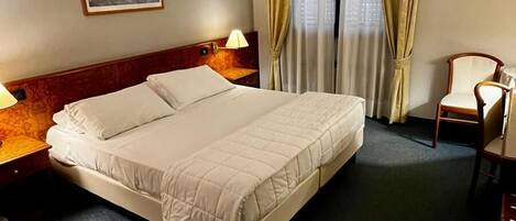A hotel room with a large bed, two bedside tables with lamps, a chair, a painting on the wall, and a window with curtains.