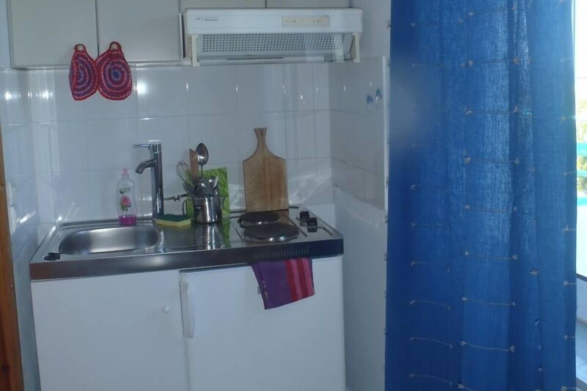 A compact kitchen with a sink, stove, and white cabinets.