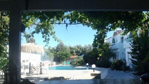 A pool area with a clear view of the sky, surrounded by trees and buildings. - SeaShell Apartments (Platanias)