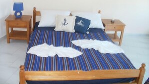 A bed with striped bedding, two pillows, and a blue lamp on a wooden nightstand. - SeaShell Apartments (Platanias)